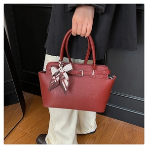 Detail of red lychee leather handbag featuring decorative buckle and silk scarf handle