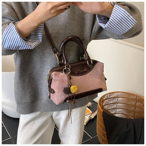 Détail du sac Boston en daim rose et cuir marron avec un pendentif pompon bicolore