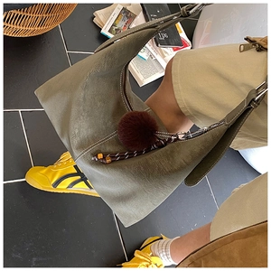 Detail view of olive green suede shoulder bag with contrast stitching and pom-pom charm