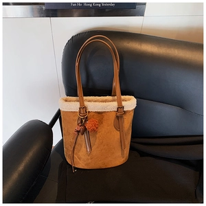 Detail of brown suede bucket bag with white faux fur trim and decorative tassel charm