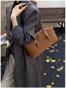 Vue détaillée d'un sac cabas marron tressé avec poignées nouées porté avec un blazer gris