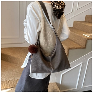 Detail of a large brown suede hobo bag with contrast stitching and plush ball charm