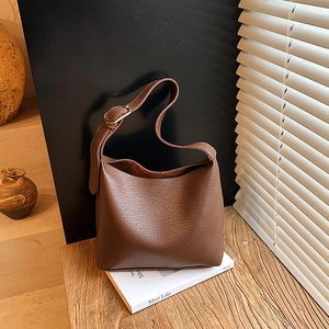 Brown litchi grain leather bucket bag with wide strap on a wooden bench setting