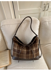 Detail of vintage brown plaid hobo bag with leather trim and bow on a cozy sofa