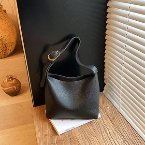 Minimalist black lychee texture leather bucket bag with golden buckle on wooden table