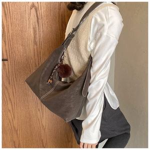 Detail of dark brown suede shoulder bag with contrast stitching and tassel charm pendant