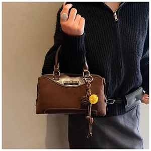 Gros plan d'un sac Boston en daim marron avec nœud en cuir et breloque pompon