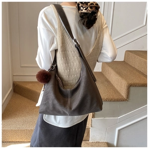 Detail of a large brown faux suede hobo bag with white stitching and plush ball charm
