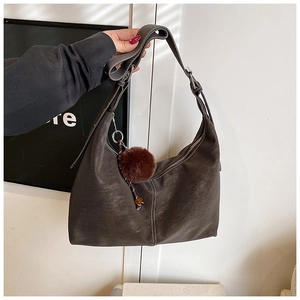 Detail of dark brown suede shoulder bag with contrast stitching and plush ball pendant