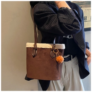 Detail of suede bucket bag with white faux fur trim and orange plush charm