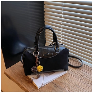 Détail du sac noir à nœud avec pompon en fourrure posé sur un banc en bois