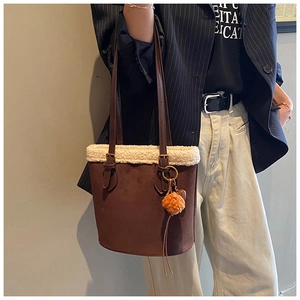 Detail of brown suede bucket bag with beige faux fur trim and orange pompom charm