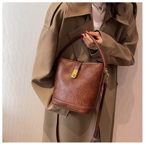 Detail of dark brown vintage bucket bag with leather texture and gold clasp on a model