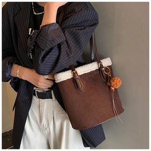 Detail of suede bucket bag featuring white faux shearling trim and orange pompom charm
