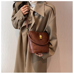 Sac seau vintage marron avec fermoir doré porté par un mannequin en trench-coat beige
