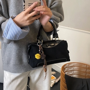 Détail du sac à main en daim noir avec breloque pompon en fourrure et anneaux métalliques