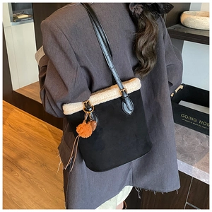 Detail of black suede bucket bag with white faux fur trim and orange pompom charm