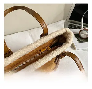 Detail of golden metal zipper and white faux fur trim on a brown suede tote bag