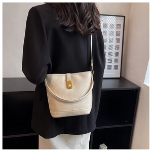 Sac seau crème chic avec texture grainée et fermoir doré porté sur un blazer noir élégant