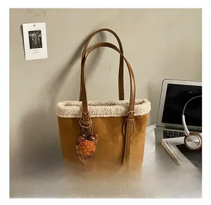 Detailed view of brown suede bucket bag with white faux shearling trim and plush pendant