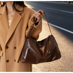 Detail of dark brown glossy leather tote bag with silver ring zipper and soft texture