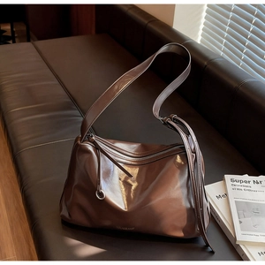 Detail of dark brown glossy leather tote bag with silver logo on a dark sofa