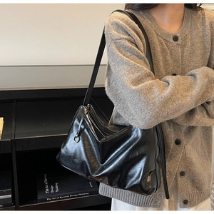 Detail of minimalist black glossy leather tote bag with soft folds and zipper closure