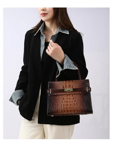 Details einer dunkelbraunen Handtasche in Krokoprägung mit goldenem Schloss an einem Model