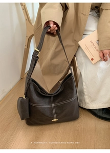 Close-up of retro brown shoulder bag with white cross-stitching and gold hardware details