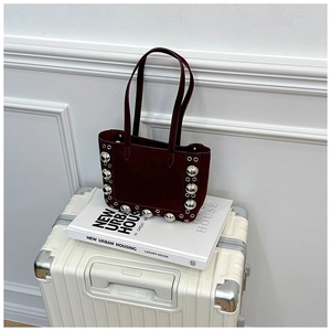 Détail du sac cabas en daim bordeaux avec clous en métal argenté sur une valise blanche