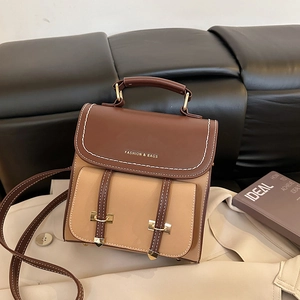 Retro-Rucksack in Kontrastfarben aus Kunstleder mit Metallgriff auf beigem Trenchcoat