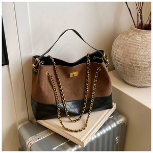 Detail of color-block tote bag with suede finish, gold lock, and chain strap on a suitcase