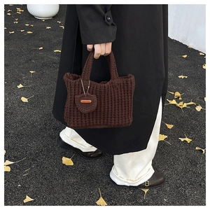 Detail of dark brown crochet handbag featuring a handmade charm on a textured knit fabric