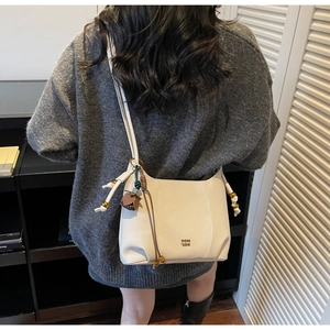 Detail of a creamy white leather crossbody bag with metal logo and fringe tassel charm