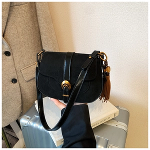 Detail of black suede saddle bag with horseshoe buckle and brown tassel charm