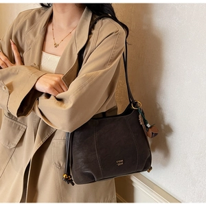 Detail of dark coffee leather shoulder bag with gold logo and drawstring accents