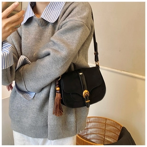 Detail of a vintage black leather saddle bag with gold clasp and tassel worn crossbody