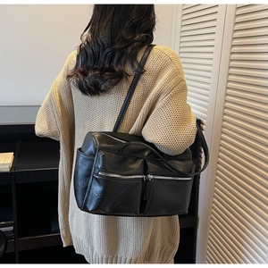 Model wearing a large black PU leather shoulder bag with multiple silver zipper pockets