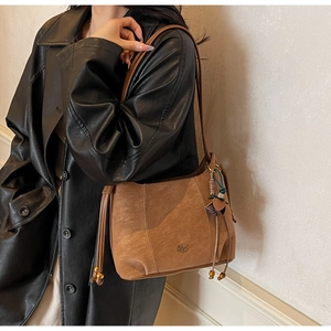 Brown vintage underarm bag with gold beads and fringe tassel detail on a leather coat