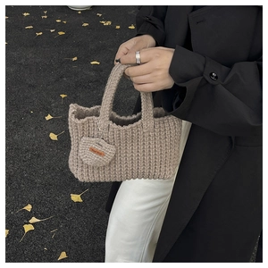 Detail of beige hand-knitted tote bag with heart charm and leather Hand Made tag
