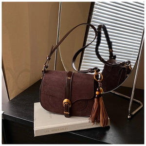 Detail of vintage coffee suede saddle bag with gold buckle and tassel on books