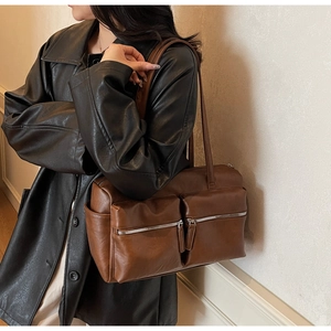 Detail of dark brown leather shoulder bag with dual front silver zippers and side pockets