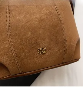 Close-up of brown pebbled leather texture with a gold metal decorative logo detail