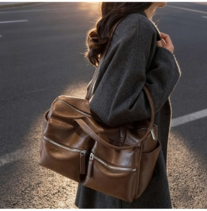 Detail of dark brown leather tote featuring dual zipper front pockets and wide handles