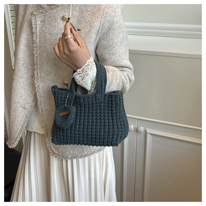 Detail view of dark green hand-knitted tote bag with chunky texture and heart charm