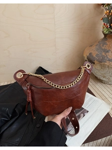 Détail d'un sac bandoulière en cuir marron avec chaîne dorée et pompon décoratif