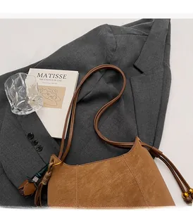 Macro shot of caramel brown faux suede hobo bag with stylish tassel detail on gray blazer