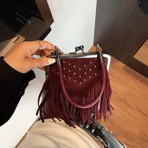 Detailed macro view of burgundy suede handbag featuring silver studs and bohemian tassels