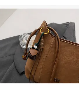 Detailed close-up of brown litchi pattern faux leather bag with flower tassel charm