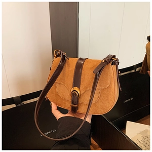 Detail of brown suede saddle bag with glossy leather strap and gold horseshoe buckle